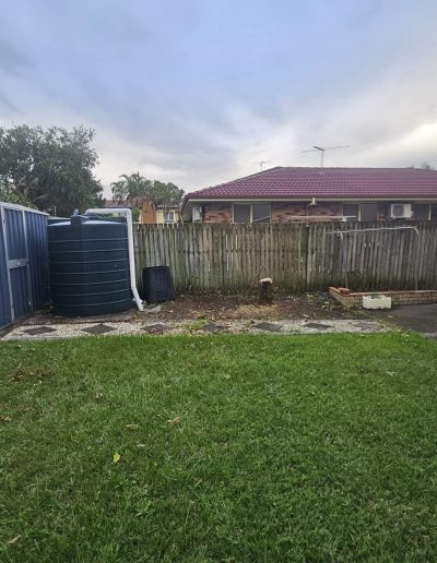 Image shows clear backyard after hedge has been removed from infront of water tank.